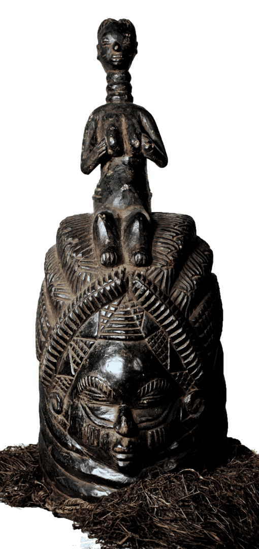 A carved, dark wooden Mende Sowei helmet mask with an ornate headdress topped by a small figure, surrounded by raffia.