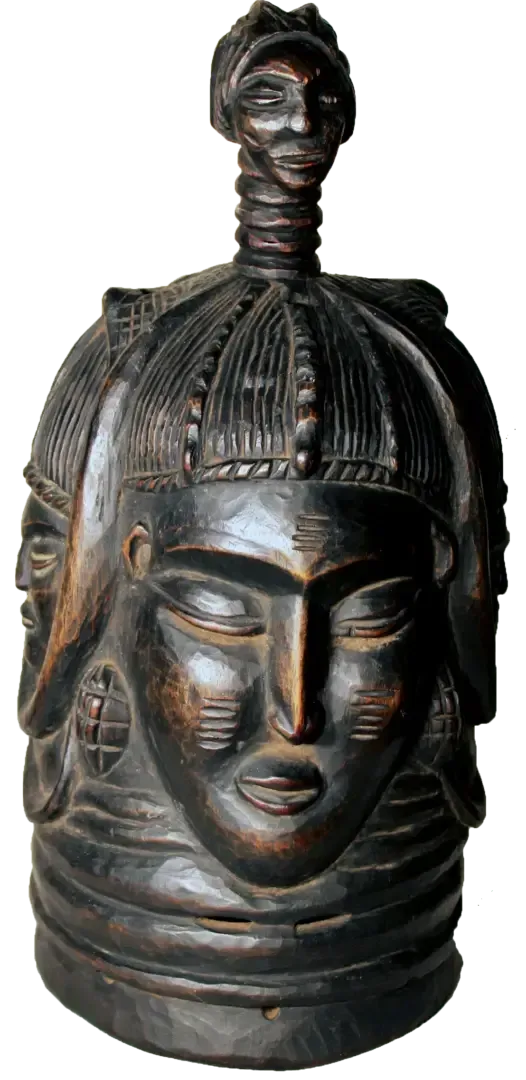 A dark wood carving of a multi-faced helmet mask with a smaller sculpted head on top, featuring intricate detailing.