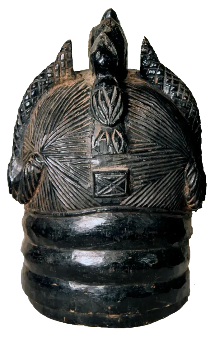 A black, carved wooden mask with three distinct peaks, intricate linear patterns on the crown, and a ridged base.