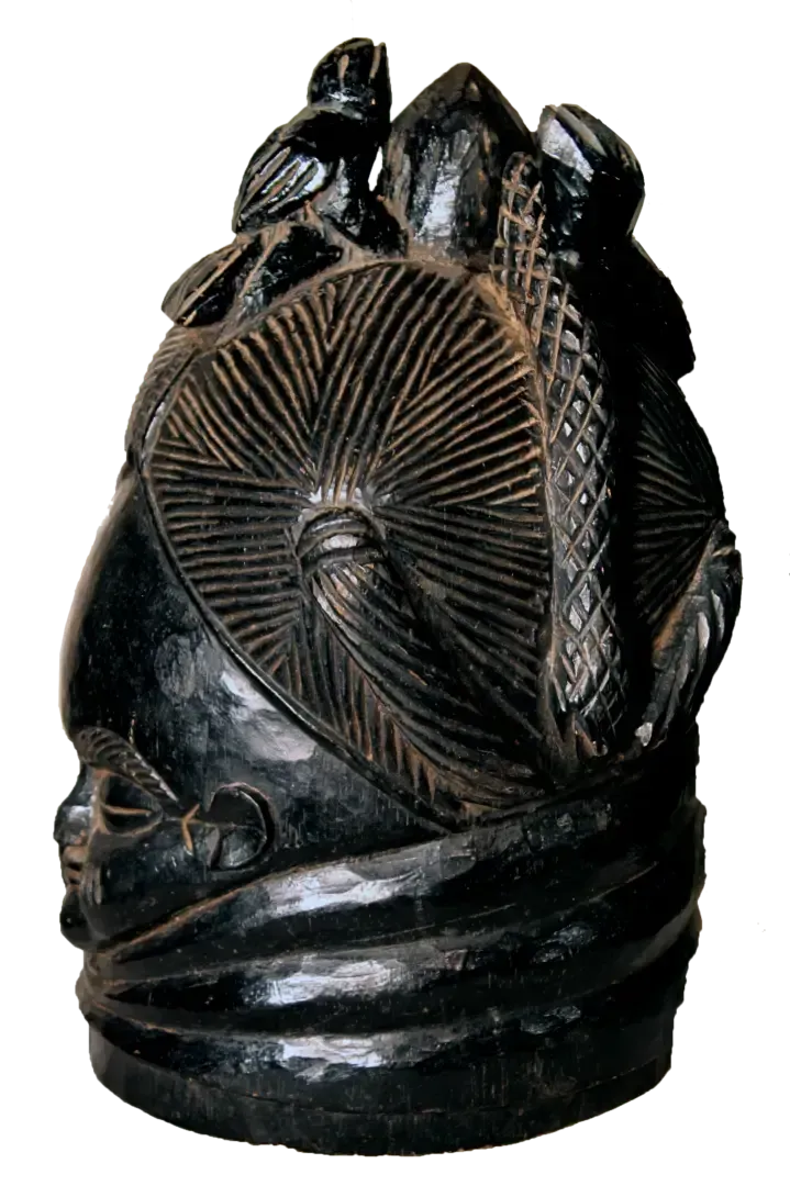 A black, polished, carved helmet mask with intricate radial patterns, topped with figures of a bird and geometric shapes.
