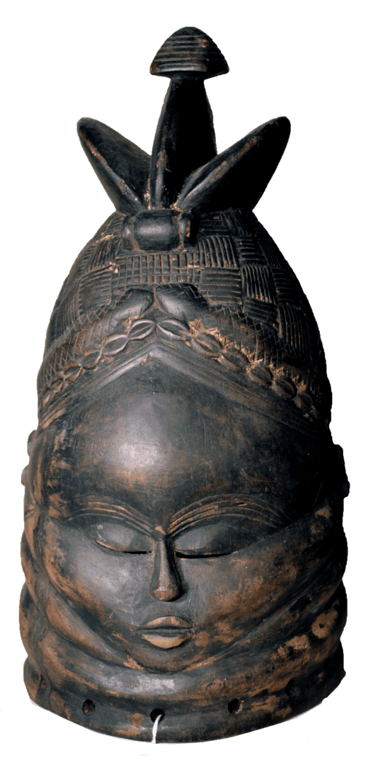 A dark, carved wooden helmet mask featuring an oval face with serene, closed eyes, intricate hair, and a tall top ornament.