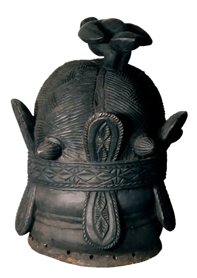 A carved wooden helmet mask with a dark, textured finish, featuring a central top crest, side projections, and patterns.