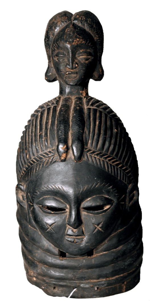 A dark, carved wooden mask with an intricate hairstyle, stylized features, and horizontal neck rings.