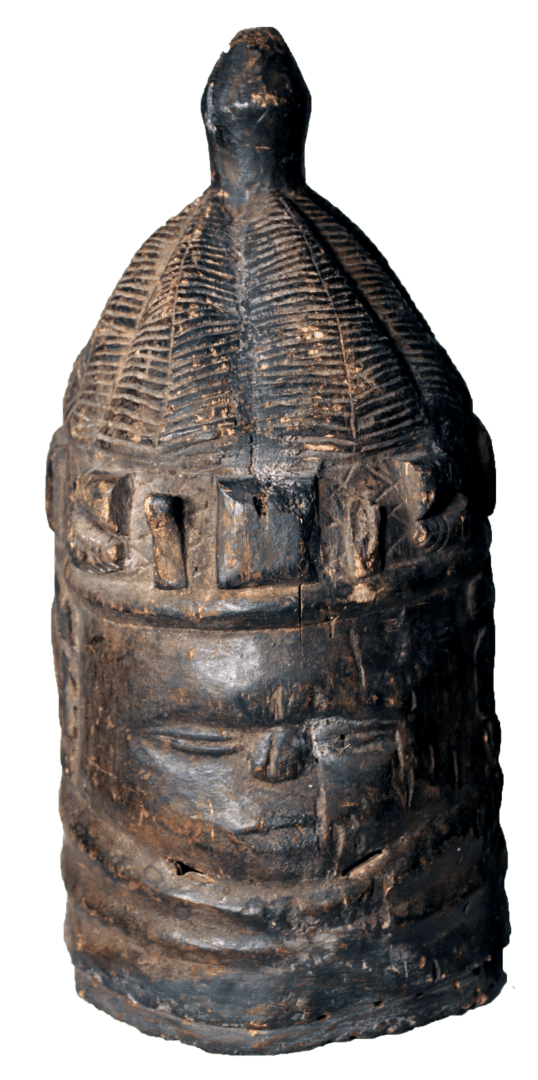 A dark, carved wooden mask with a textured, domed crown, human facial features, and horizontal neck rings.