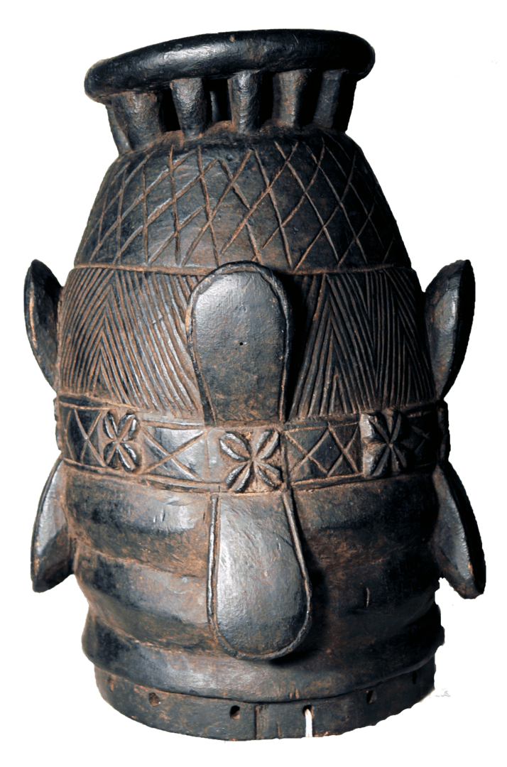 A dark, carved wooden mask with geometric patterns, projecting petal-like shapes, and a cylindrical top rim.