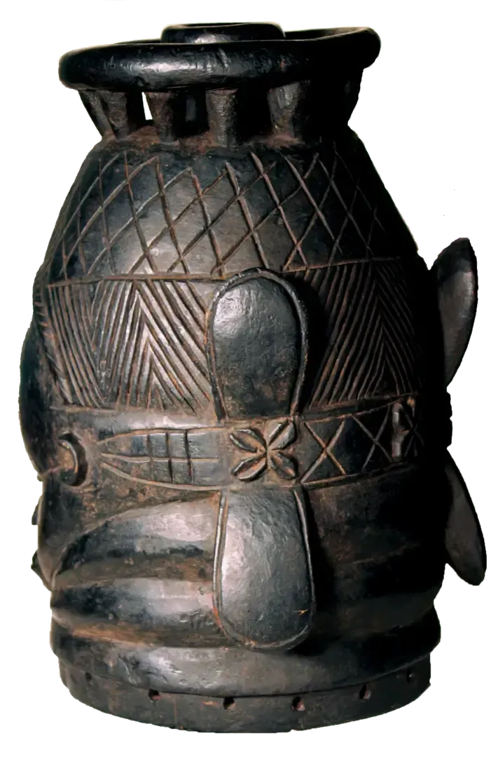 A dark, cylindrical wooden drum with a carved geometric lattice pattern and four raised paddle-like protrusions.