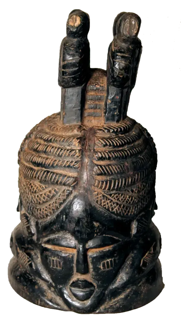 A carved dark wooden Mende helmet mask with an ornate, textured hairstyle featuring two small standing figures on top.