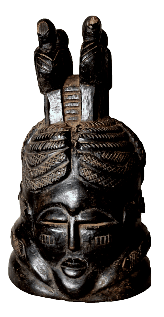 A dark, carved wooden helmet mask featuring an ornate braided hairstyle topped with two small, stylized figures.