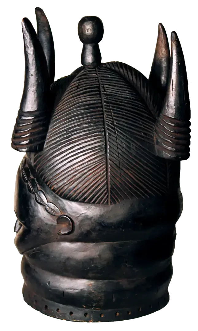 A dark, carved wooden helmet mask featuring patterned hair, a central knob, and four symmetrical, horn-like projections.