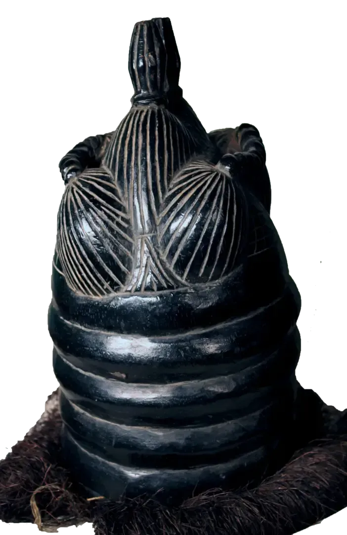 A black, carved wooden Mende Sowei helmet mask with ringed neck, intricate coiffure, and raffia fringe at the base.