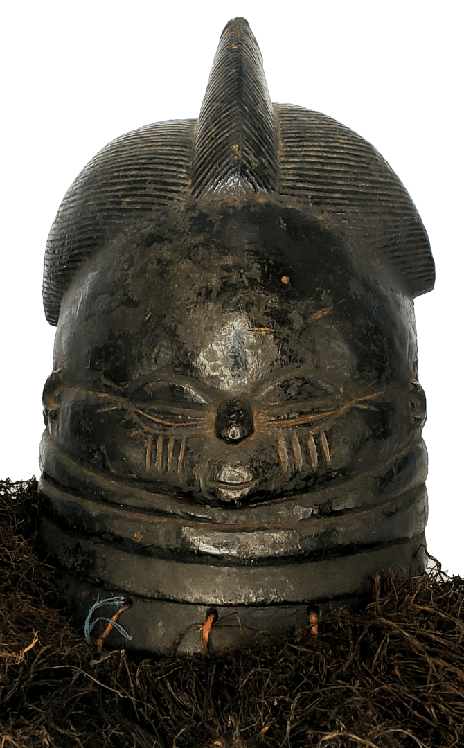 A dark, polished wooden Mende Sowei mask with a detailed, stylized face and hair, resting on a base of dark raffia fibers.