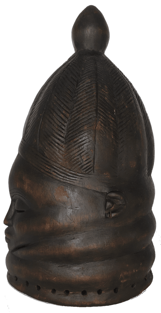 A dark, carved wooden mask with an intricate chevron-patterned hairstyle and a series of holes along its base.