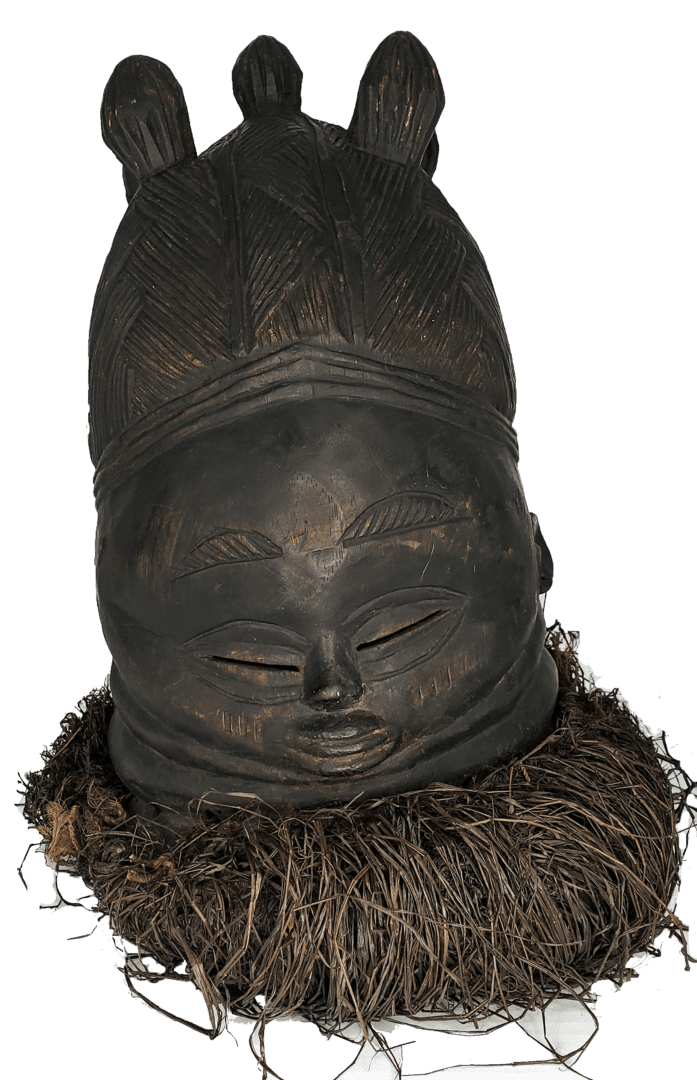 A carved wooden mask with an intricate hairstyle, closed eyes, small mouth, and a collar of dark fibrous material.