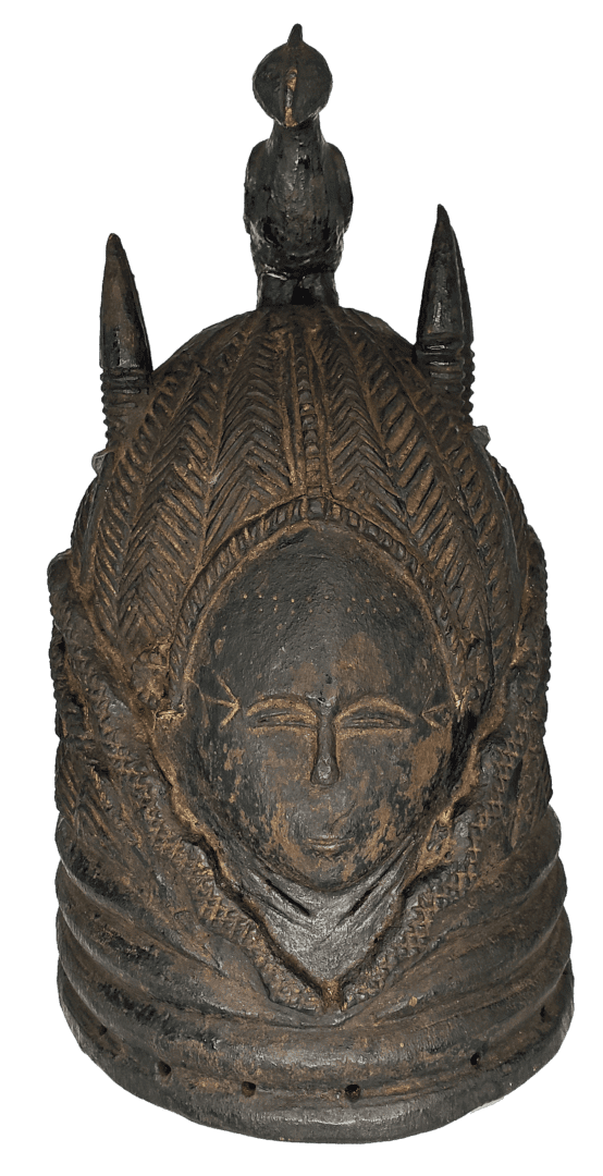 A carved, dark wooden helmet mask featuring a central face, ridged patterns, and a bird-like figure perched on top.
