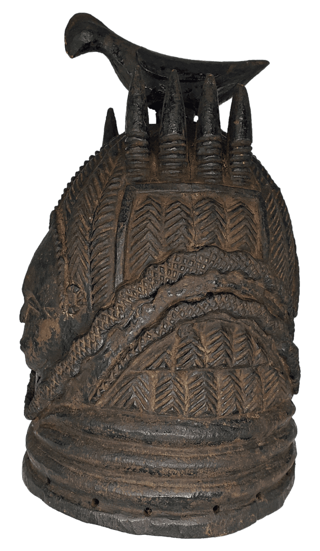 A dark, intricately carved wooden ceremonial helmet featuring a perched bird figure at the top and ornate tribal patterns.