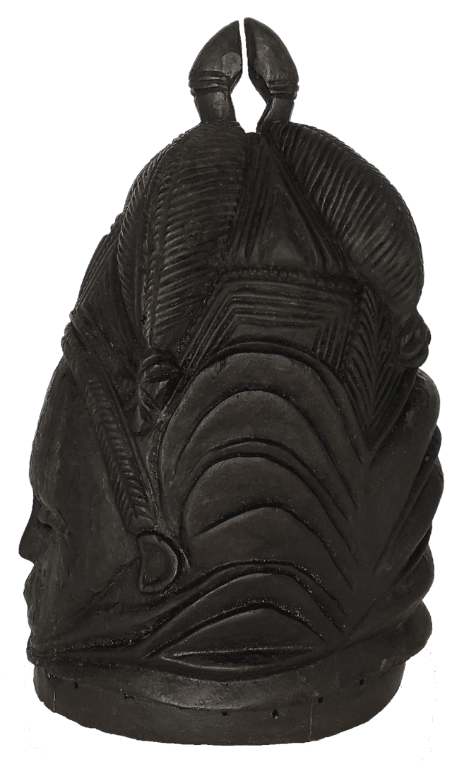 A dark, carved wooden helmet mask featuring stylized, layered patterns and a pair of rounded, protruding shapes on top.