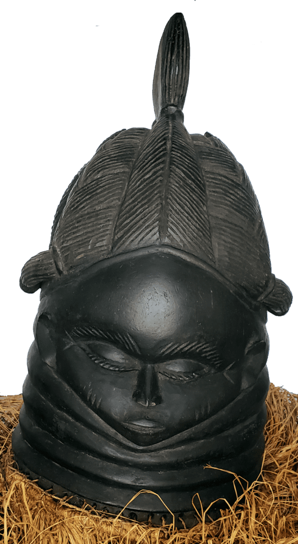 A black, carved wooden Mende Sowei helmet mask with a stylized hairstyle, resting on a bed of raffia straw.