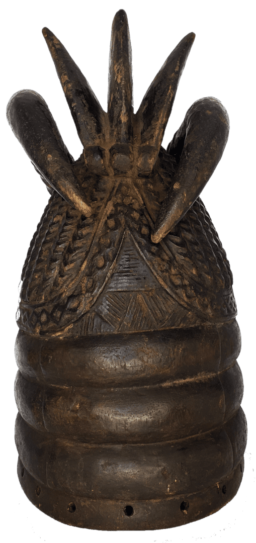 A dark, cylindrical wooden headdress featuring carved textures, patterned motifs, and five prominent upward-facing spikes.