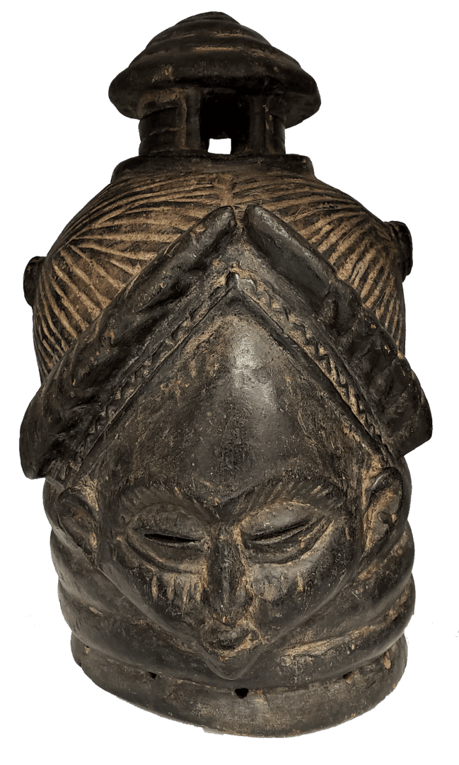 A dark, carved wooden mask with an intricate, textured headpiece, prominent brow, and small, closed eyes.