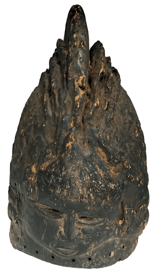 A weathered, dark-colored carved wooden helmet mask with a prominent, textured crest and small, carved facial features.