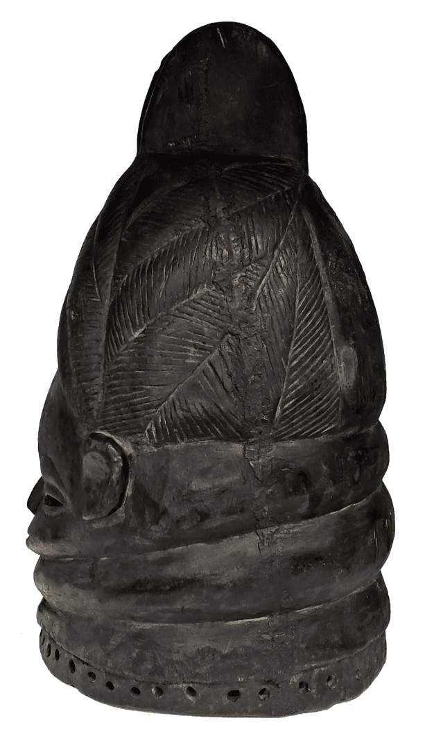 A dark, carved wooden helmet mask featuring textured patterns, circular motifs, and a rounded, dome-like top.