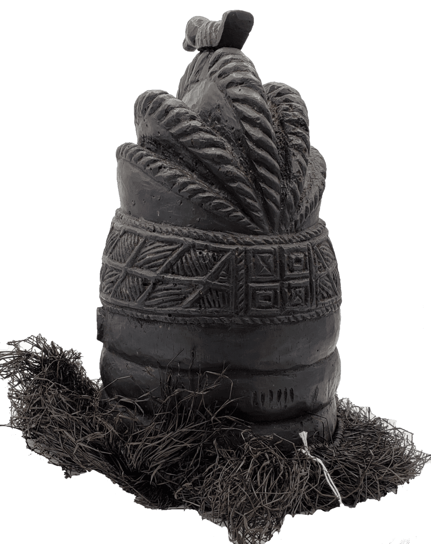 A dark-colored, cylindrical carved artifact with decorative geometric patterns and fibrous material at the base.