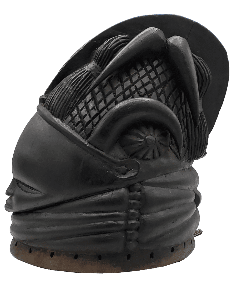 A carved black wooden mask featuring detailed patterns, a prominent curved arch over the eye, and a layered base.