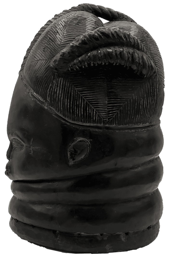 A dark, carved wooden mask with a complex, textured hairstyle and multiple horizontal ridges encircling the neck.