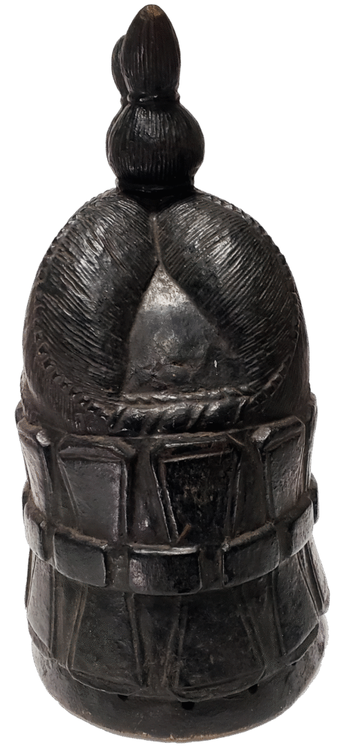 A dark, carved wooden helmet or headpiece featuring a textured crown, a protruding top knob, and a horizontal band detail.