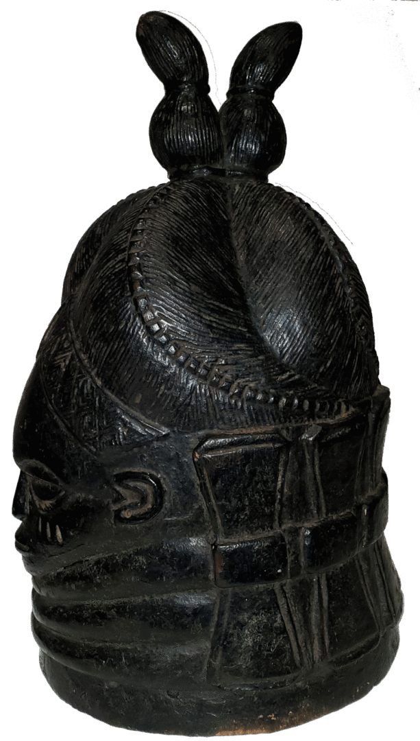 A black, carved wooden helmet mask featuring elaborate patterned hair, facial features, and a textured, grid-like base.
