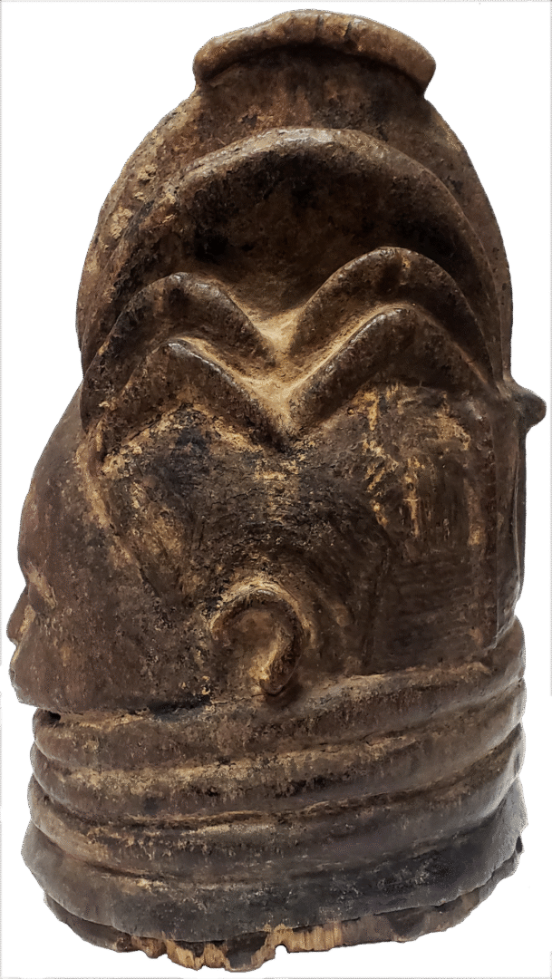 A dark, carved wooden object featuring a stylized head with layered, patterned hair and ridged neck rings.