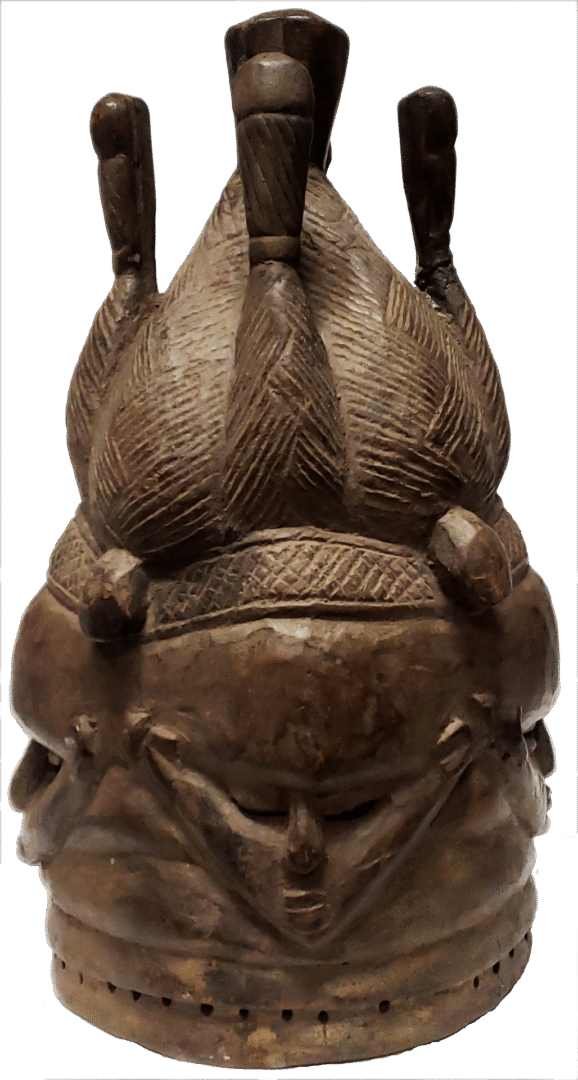 A carved wooden helmet mask featuring three stylized figures atop a textured, multi-faced cylindrical base.