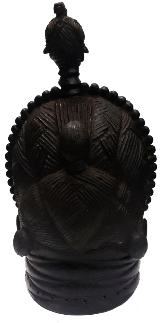 A dark, carved wooden ritual headdress featuring a central figure surrounded by a textured, fan-like semi-circle.