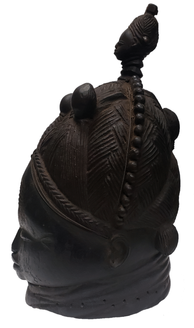 A dark, carved wooden mask with a textured headdress featuring geometric patterns, rounded protrusions, and a top finial.