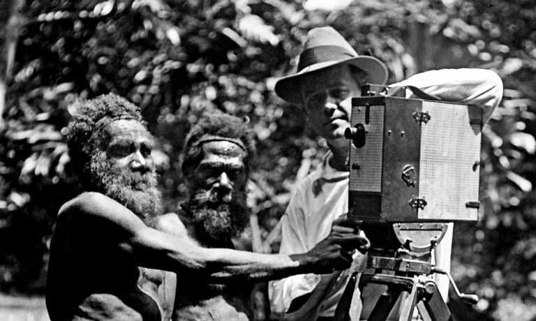 A person with a vintage film camera on a tripod next to two individuals in a wooded area.