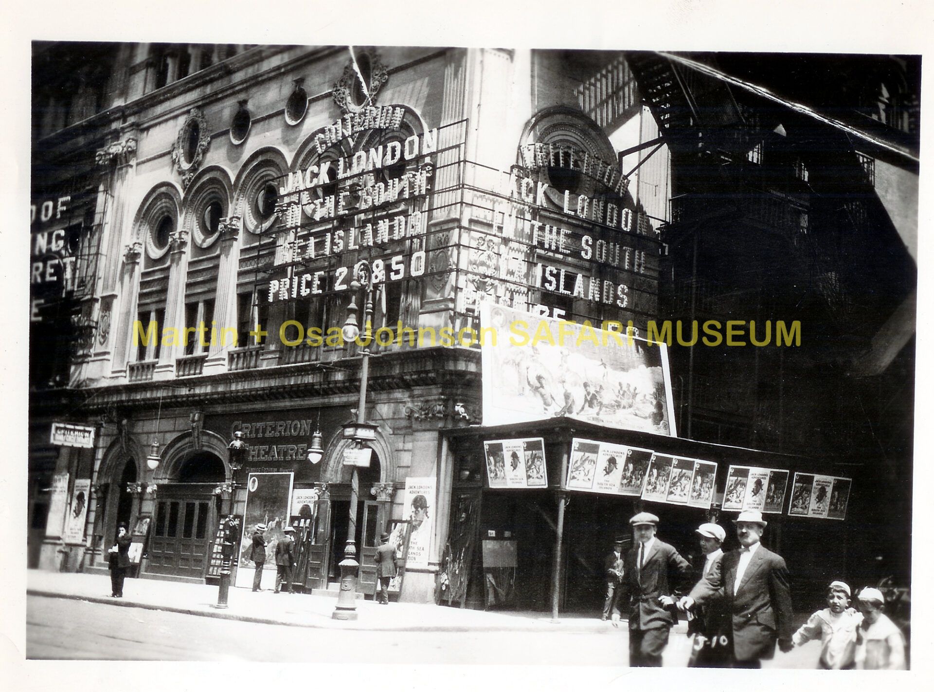 A black-and-white street-level view of a theater marquee advertising a Jack London film, with people walking on the sidewalk.