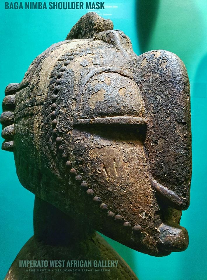 A side-profile view of a weathered, wooden Baga Nimba shoulder mask against a bright teal background.