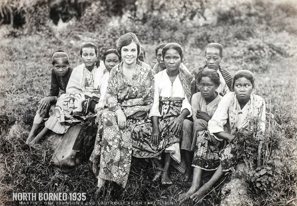 A group of people sitting together in a field in North Borneo, 1935, with one person centered among them.