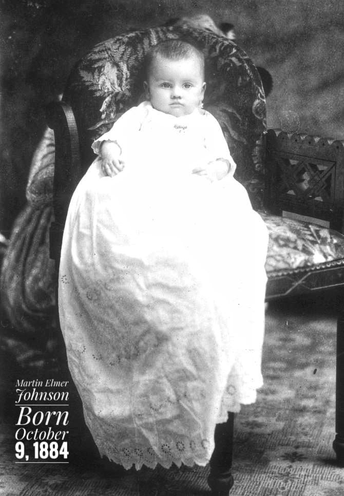 A portrait of an infant wearing a long, lace-trimmed gown, seated on a patterned chair. Text reads 