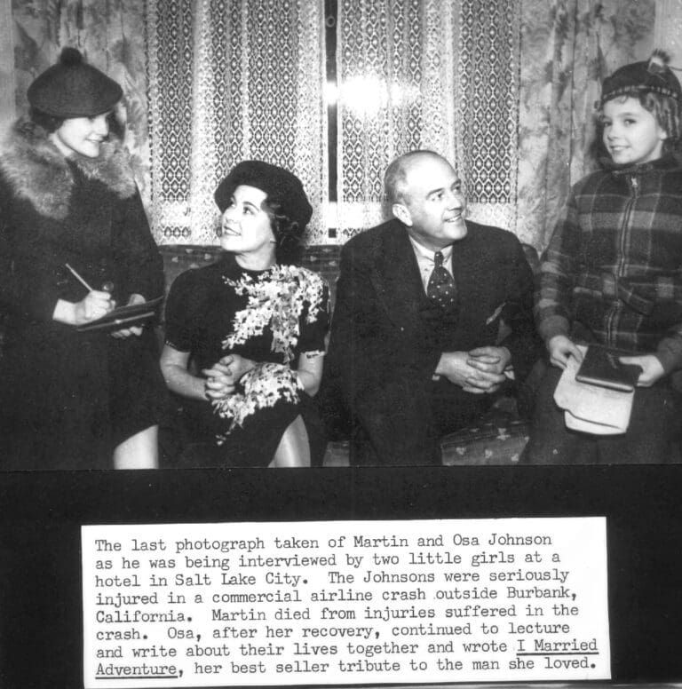 Martin and Osa Johnson sit with two girls interviewing them in a hotel, with an informational caption below the photo.