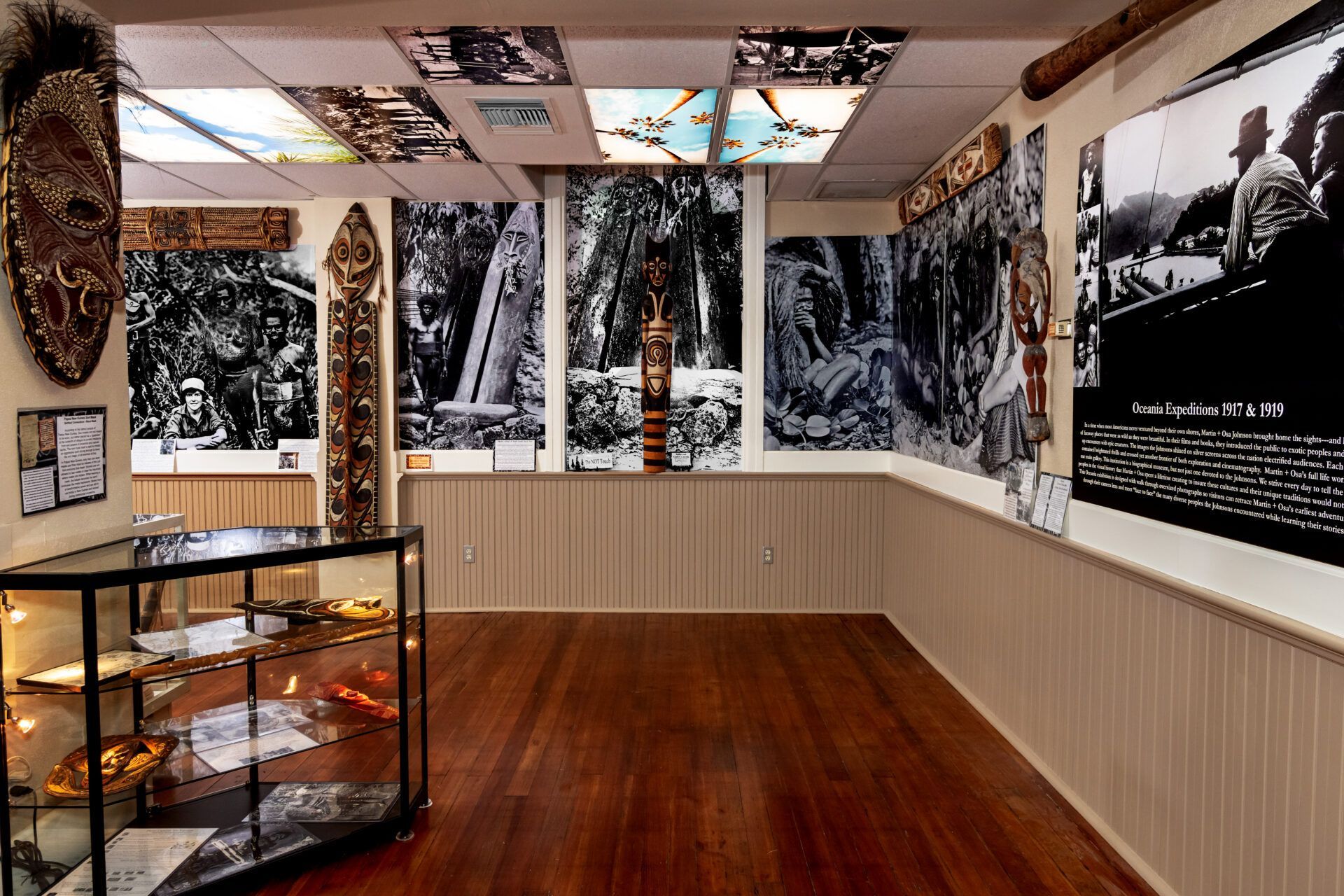 Museum room with wood floors, glass display cases, and large black-and-white photographic murals depicting cultural history.