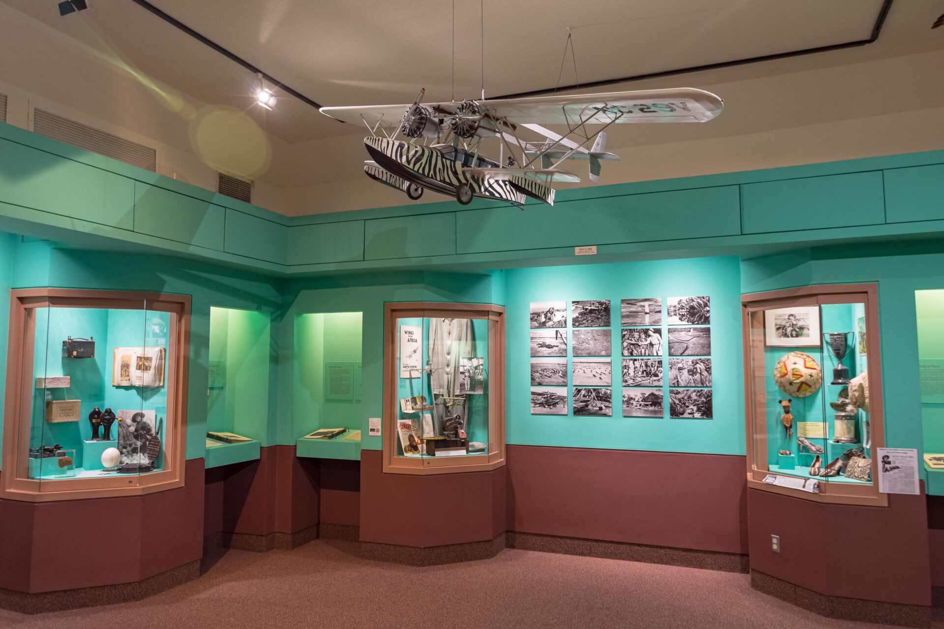 A museum display with a hanging model aircraft above, featuring three glass cases containing historical artifacts.