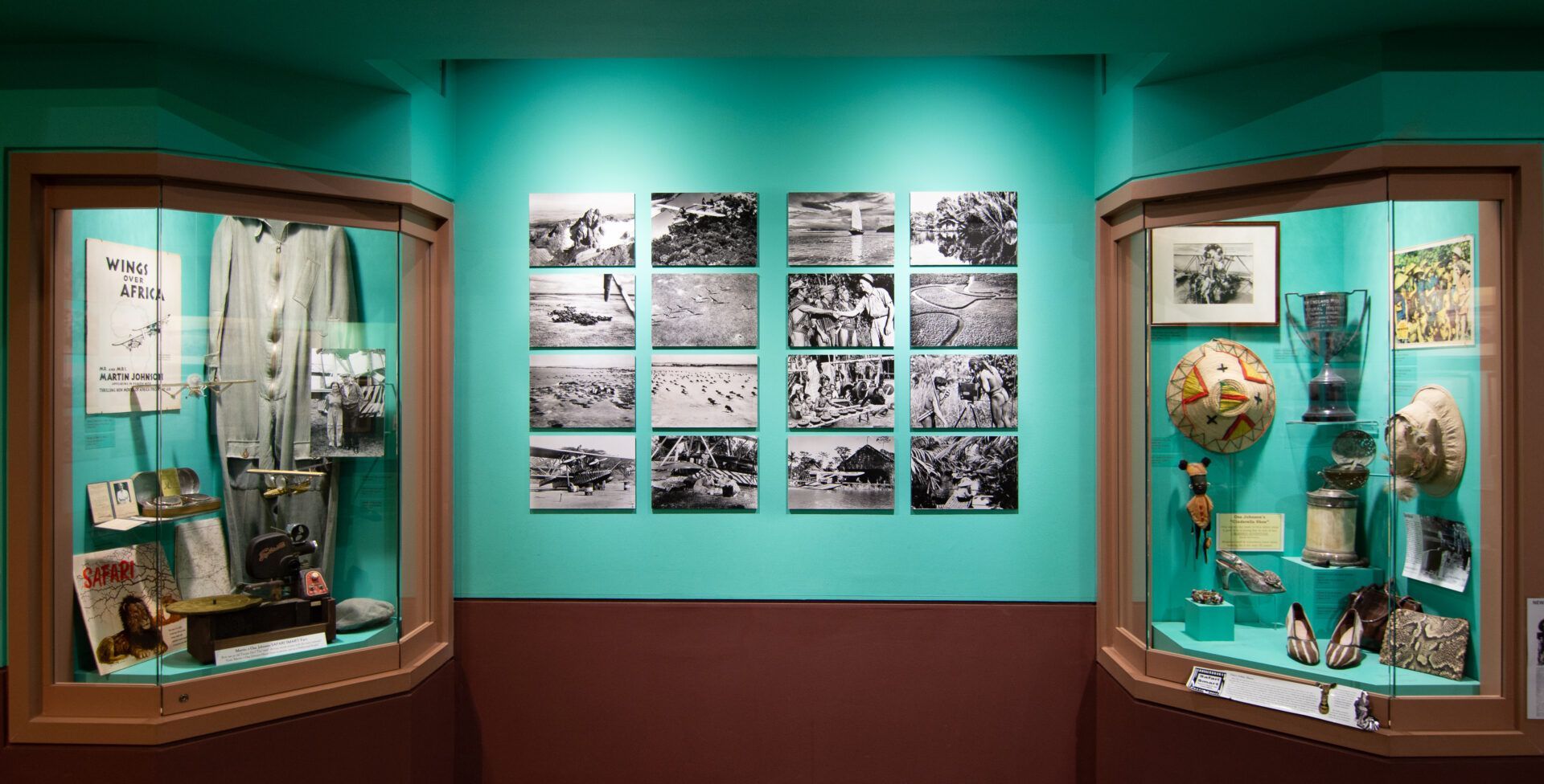 A museum exhibit featuring two glass display cases with artifacts, flanking a wall grid of sixteen black-and-white photos.