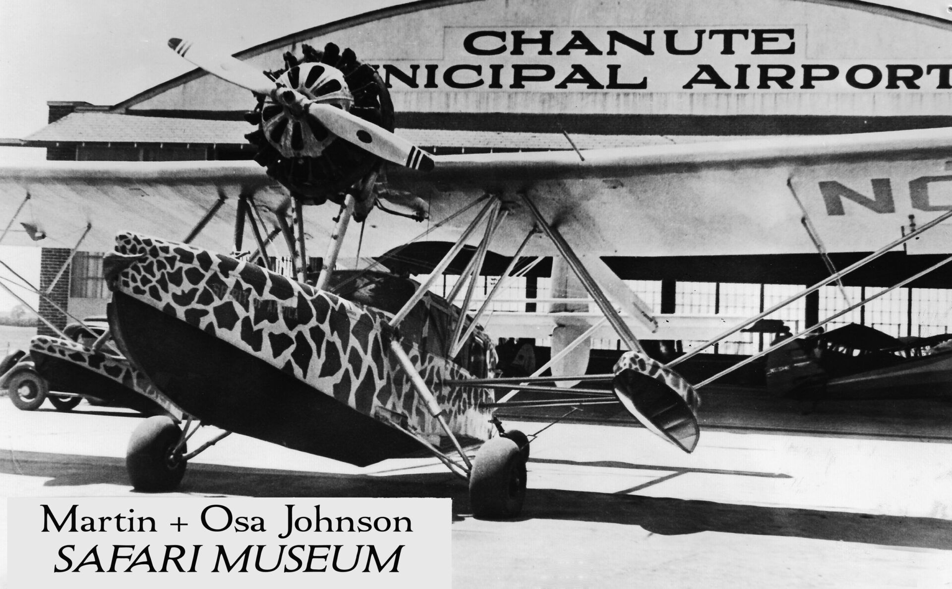 A vintage, giraffe-patterned seaplane parked in front of the Chanute Municipal Airport.