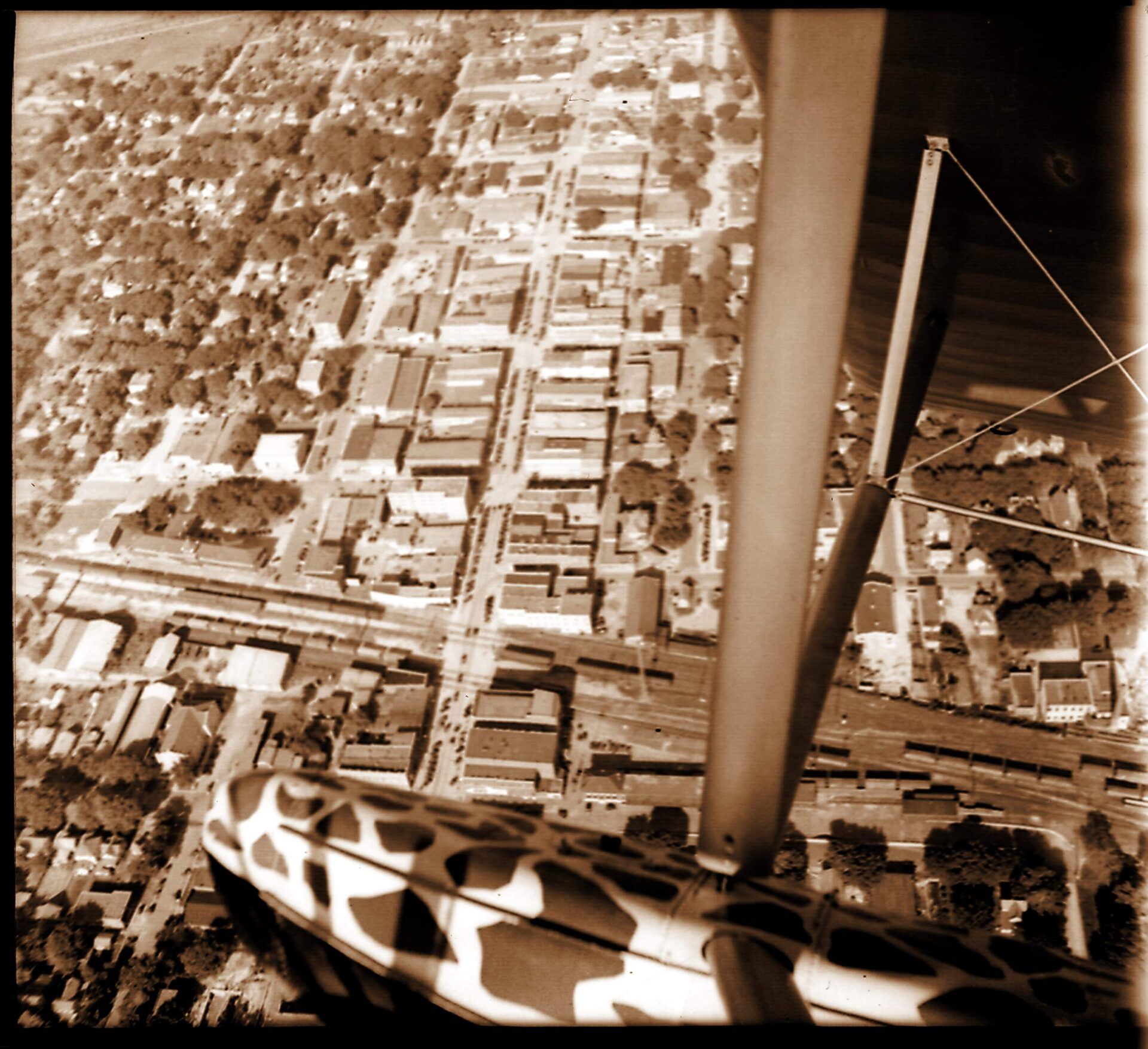 Aerial view of a small town street grid taken from an airplane, featuring wing struts in the foreground.