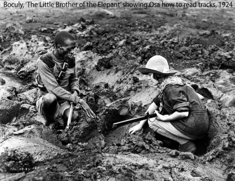 A person points to footprints in the mud while another individual watches, in a 1924 photograph titled 