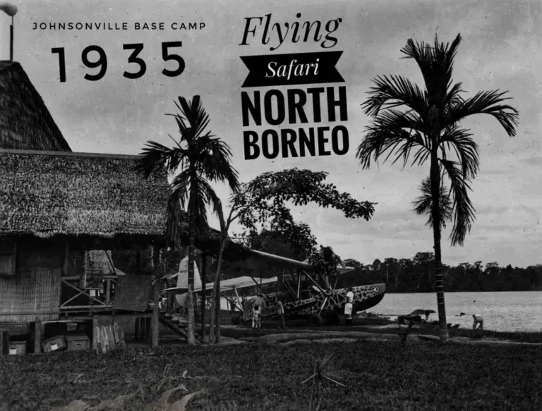 A vintage black-and-white photo of a riverside base camp in North Borneo in 1935, featuring a seaplane and palm trees.