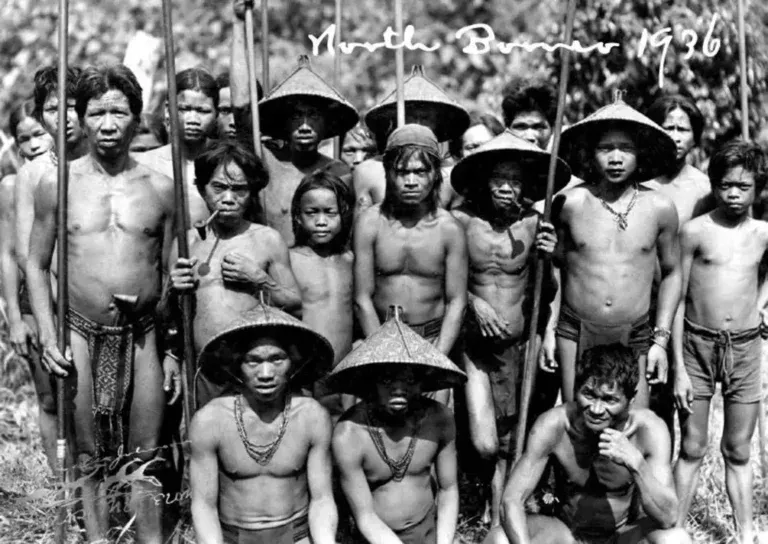 A 1936 archival photo of North Borneo people standing with spears and wearing conical hats.