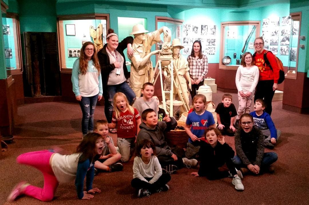 A group of children and adults posing together inside a museum exhibit featuring life-sized sculptures.