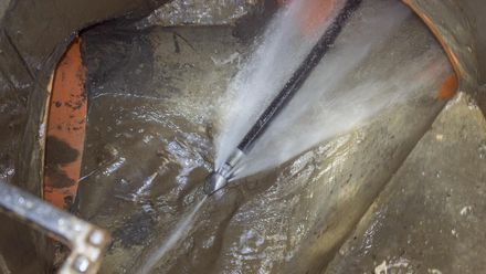 Close-up of a metal surface being pressure-washed, with water spray and a hose visible.